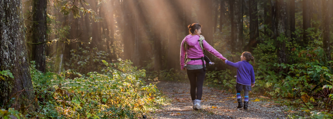 A mother holding her daughter's hand walking in the woods.