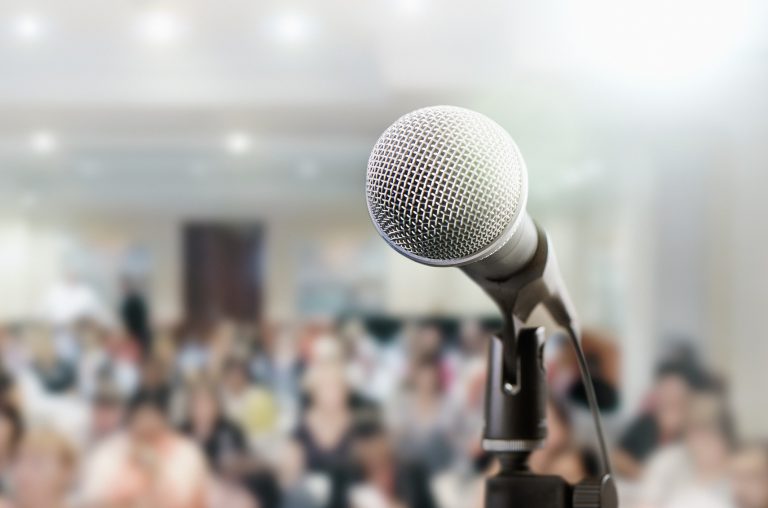 Audience sits waiting for the speaker at a conference. The microphone is in the foreground.