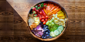 A bowl full of colorful fresh fruit and vegetables on a wooden table
